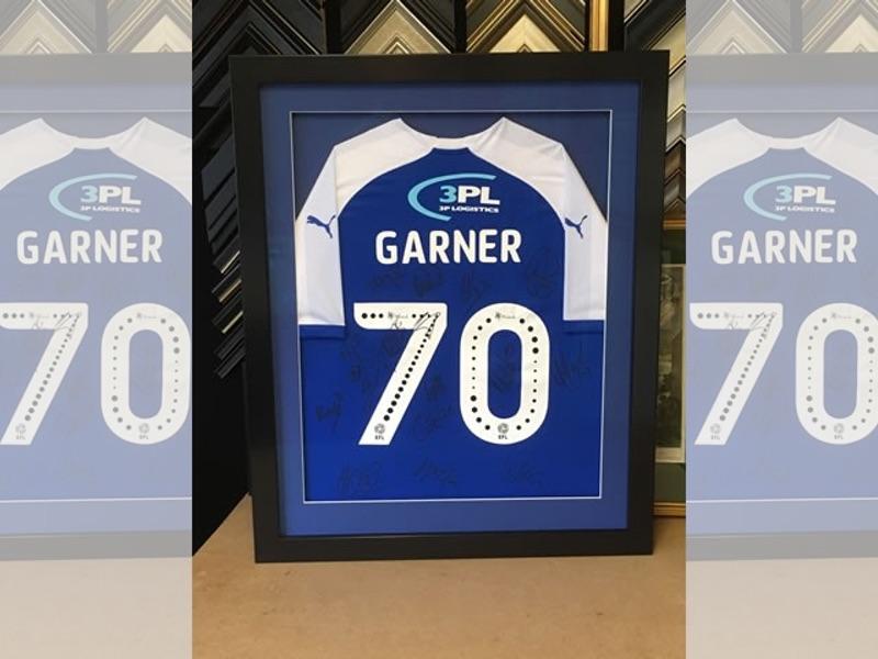 A signed Wigan Athletic shirt, framed in a black gloss box frame and glazed with Tru Vue reflection control glass.